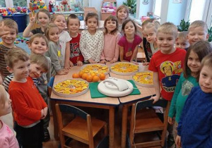 Dzieci stoją przy stole, na którym przygotowały pomarańcze do suszenia.